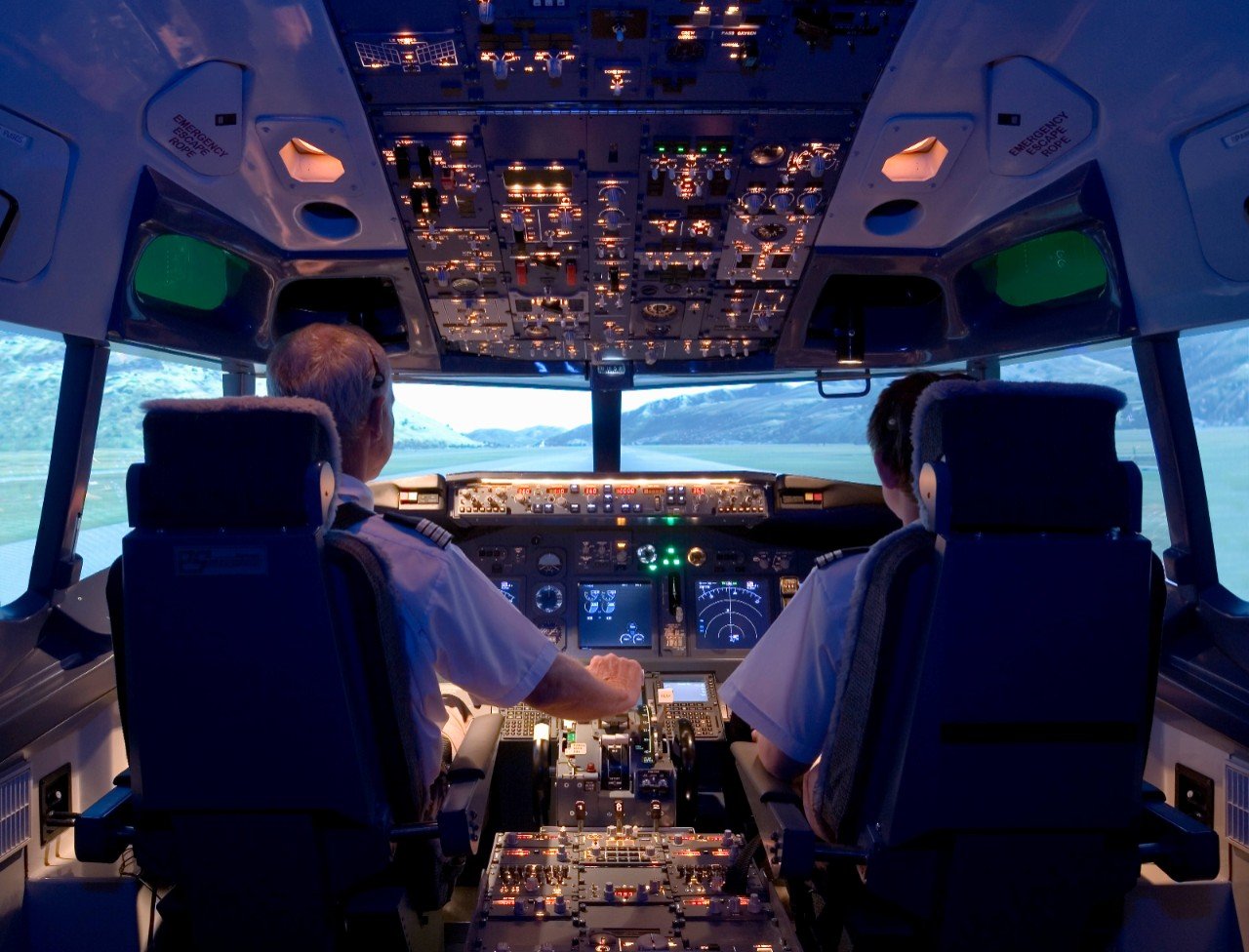 Two pilots sat in a commercial airliner cockpit at the base of a runway.